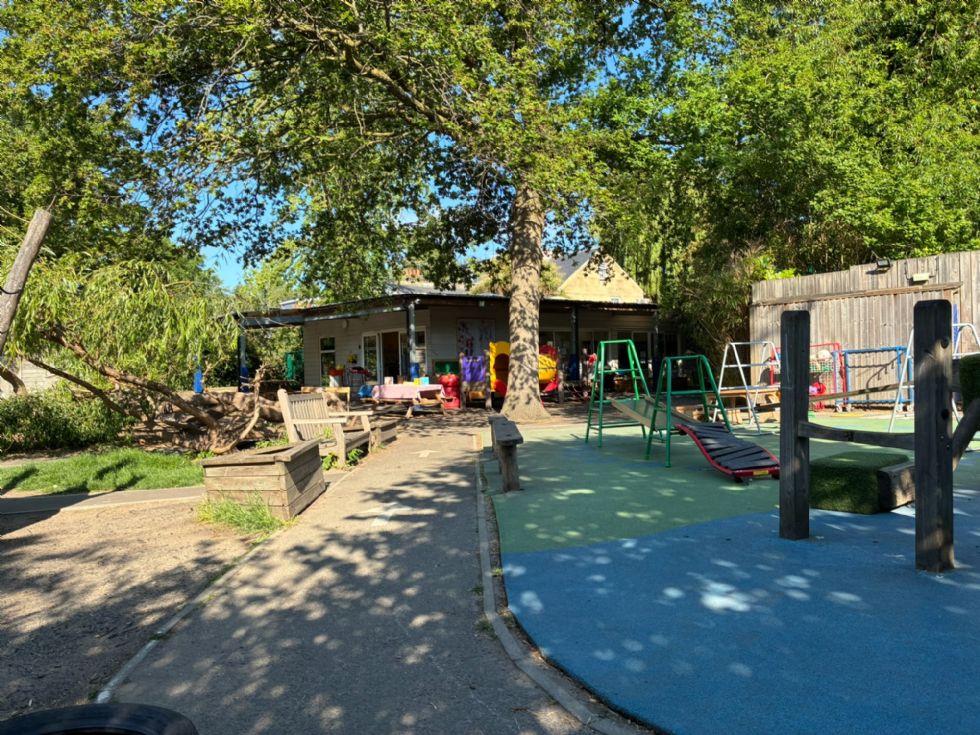 On the right is lots of climbing equipment. In the distance on the left is the climbing tree, the trunk of the huge oak tree, and the single-story, white clapboard nursery building. 