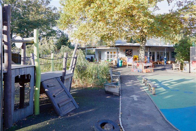 Sunny day. Church Hill garden showing the pirate ship climbing frame, the willow climbing tree and the racing track. In the background is the single-storey nursery building.