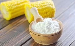 cornflour two cobs of sweetcorn behind a wooden bowl filled with cornflour and with a wooden scoop sticking into the flour